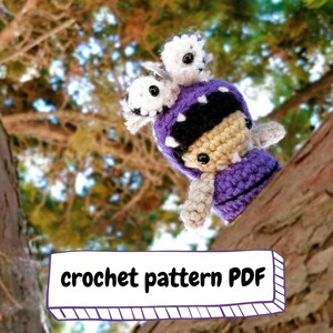 Puede incluir: Patrón de crochet PDF para un juguete amigurumi monstruo morado y negro con ojos blancos. El juguete está sentado en una rama de árbol.
