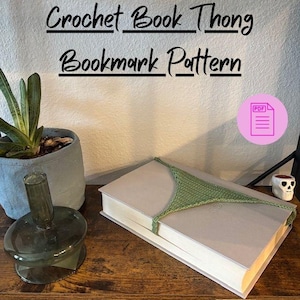 以下が含まれることがあります： 緑色のクロシェ編みのTバック型ブックマークが閉じられた本の上に置かれています。「Crochet Book Thong Bookmark Pattern」というテキストが画像上部にあります。PDFアイコンも表示されています。