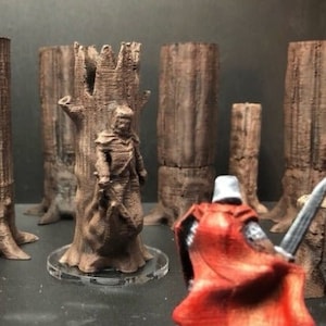 May include: A miniature figure of a knight in red armor stands in front of a collection of brown, textured, tree trunk-shaped miniature scenery pieces. The knight is holding a sword and is wearing a red cape.