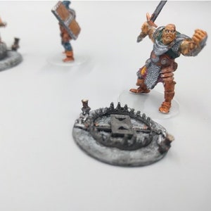 May include: Three miniature figures on circular bases, one with a sword and shield, one with a sword and a trap, and one with a trap. The figures are painted in shades of brown, orange, and grey.