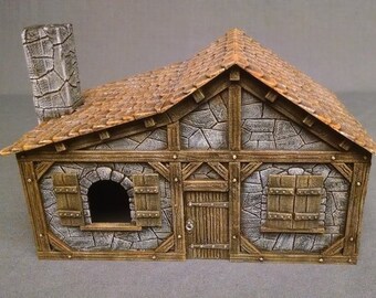 May include: A miniature model of a stone cottage with a brown shingled roof and a chimney. The cottage features wooden beams, shutters, and a front door. The stone walls are gray, and the overall design is rustic.