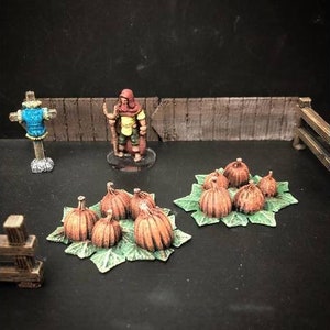 May include: A miniature figure of a person wearing a red hooded cloak and holding a staff stands in front of a wooden fence.  There are two groups of miniature pumpkins on green leaves in front of the figure.