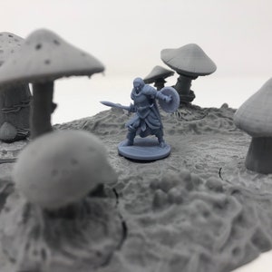 May include: A gray plastic miniature figure of a warrior holding a spear and shield standing on a gray plastic base. The figure is surrounded by gray plastic mushrooms.