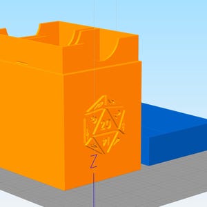 May include: An orange dice box with a 20-sided die design on the front. A blue rectangular box is next to the dice box. The dice box has a slot on top for easy access.