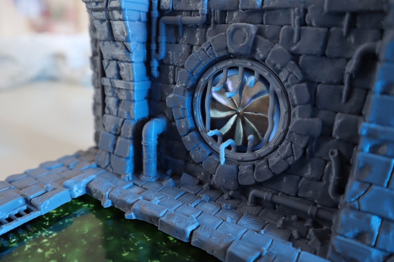 May include: A 3D printed model of a stone building with a large, round window featuring a metal fan. The building has a blue and gray color scheme and is set against a blurry background.
