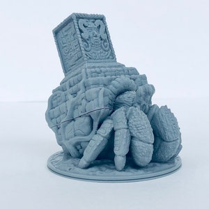 May include: A gray 3D printed miniature of a crab carrying a stone structure on its back. The structure is decorated with intricate carvings and a face on the front.