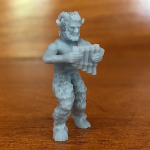 May include: A gray 3D printed figurine of a satyr playing a pan flute. The satyr has horns, a beard, and is wearing a loincloth.