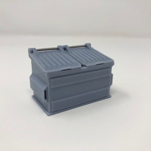 Peut inclure: Une poubelle en plastique grise avec deux couvercles et une poignée en métal.