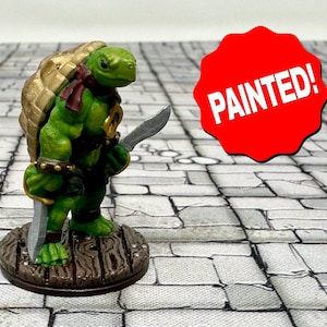 May include: Painted miniature figurine of a green turtle warrior holding a sword. The turtle is wearing a gold and brown shell, a red bandana, and a gold belt. The figurine is standing on a brown wooden base.