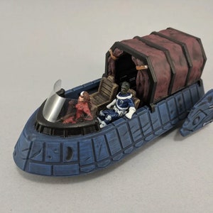 May include: A blue and black miniature spaceship with a red and black figure in the cockpit and a green and blue figure in the passenger seat. The spaceship has a dark red fabric canopy.