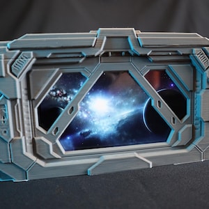 May include: A grey 3D printed box with a window showing a nebula and planets. The box has a futuristic design with raised edges and details.