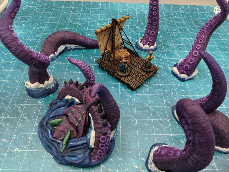 May include: Purple and blue painted miniature kraken with tentacles reaching out of the water. The kraken is attacking a small wooden raft with a treasure chest and a miniature figure on it.