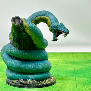 Peut inclure: Une miniature en plastique verte et bleue d'un serpent à deux têtes avec la bouche ouverte, enroulé autour d'un tronc d'arbre. La miniature est sur une base ronde.