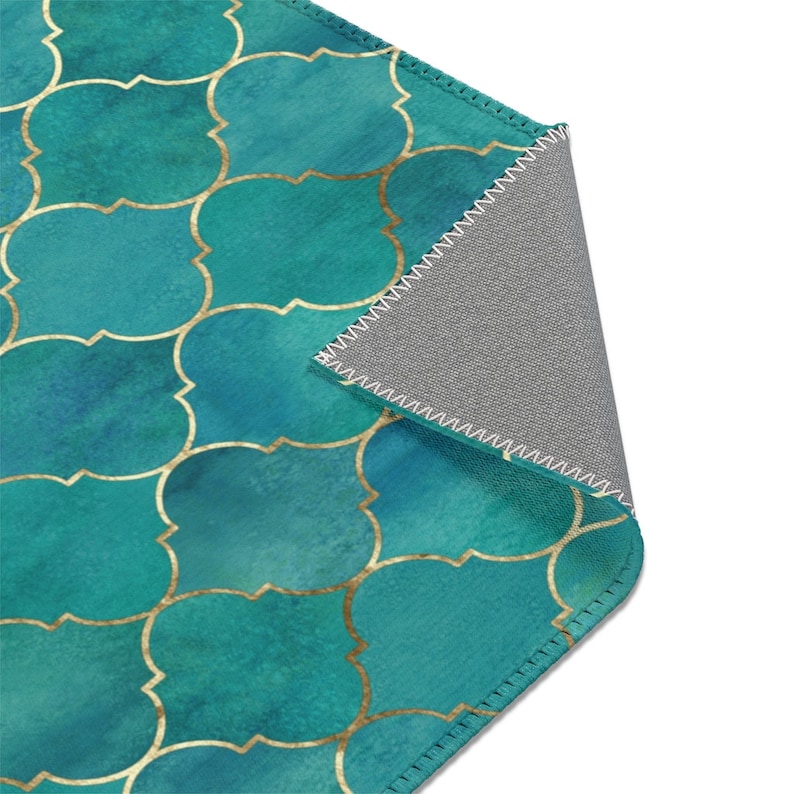 May include: A teal and gold geometric patterned rug with a gray backing. The rug has a stitched edge.