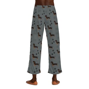 May include: Gray lounge pants featuring an all-over pattern of black and tan dachshund dogs, black paw prints, white dog bone outlines, and white food bowl outlines. The pants have a straight-leg cut and an elasticized waistband at the top.