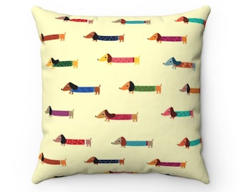 May include: A yellow throw pillow with a repeating pattern of dachshunds wearing colorful sweaters. The dachshunds are facing different directions and have different colored sweaters.
