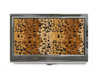 May include: A silver metal business card holder with a leopard print design. The print features a repeating pattern of brown, orange, and black spots.