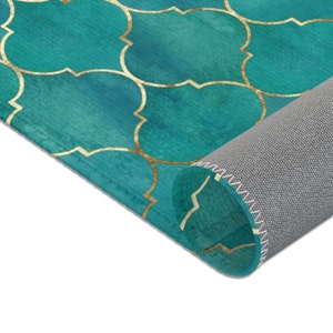 May include: Teal and gold area rug with a geometric pattern. The rug is rolled up, showing the gray backing and stitched edges.