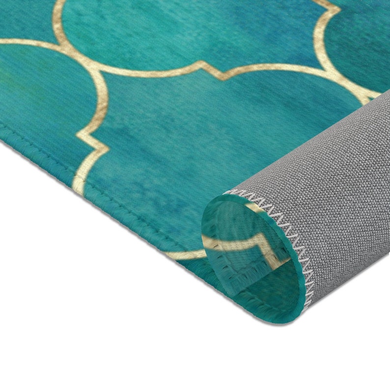 May include: A teal blue rug with a gold geometric pattern. The rug is rolled up, showing the gray backing.