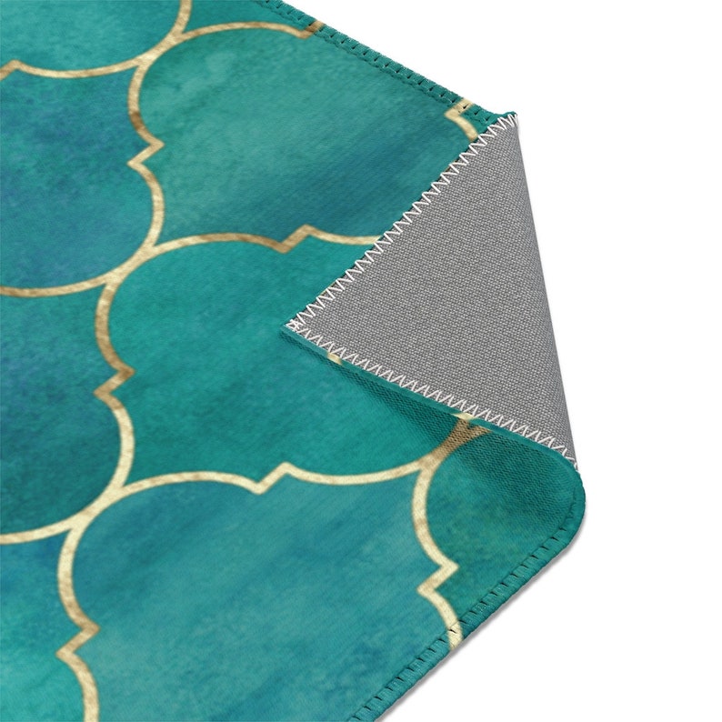 May include: Teal and gold patterned rug with a geometric design. The rug has a gray backing and is edged with white stitching.
