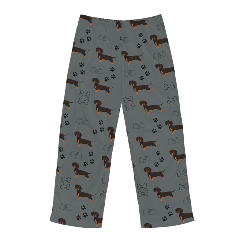 May include: Gray lounge pants featuring an all-over repeating pattern of black and tan dachshund dogs, black paw prints, white dog bones, and light gray dog bowls. The pants have a straight-leg cut and a simple elasticized waistband design.