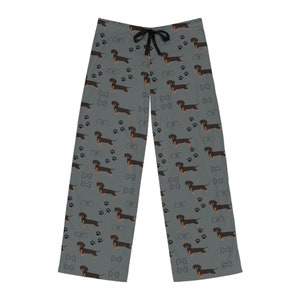 May include: Gray pajama pants featuring an all-over pattern of black and tan dachshund dogs, black paw prints, white dog bones, and gray food bowls. The pants have a black drawstring at the elastic waistband and a straight-leg silhouette.