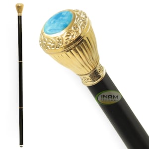 Puede incluir: Un bastón negro con un mango dorado y una piedra azul en la parte superior. El mango está decorado con un diseño floral.