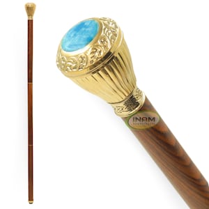 Puede incluir: Un bastón de madera con una parte superior dorada que presenta una piedra preciosa azul. La parte superior está diseñada de forma intrincada con un patrón floral. El bastón está hecho de madera oscura con veta natural.