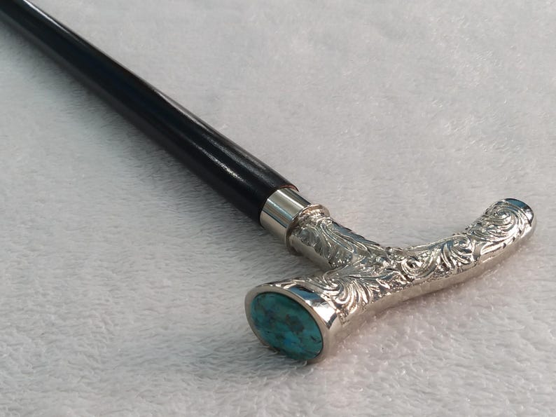 Puede incluir: Un bast&oacute;n de madera negro con un mango de plata y una incrustaci&oacute;n de piedra turquesa. El mango est&aacute; adornado con un dise&ntilde;o floral.