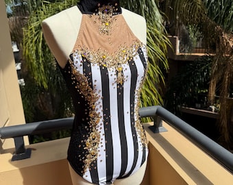 May include: A black and white striped leotard with gold embellishments. The leotard has a high neck with a black velvet collar and a tan mesh panel. The design includes gold-colored rhinestones and decorative patterns.