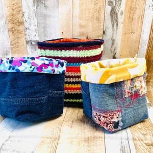 May include: Three denim storage baskets with different fabric linings. One basket has a colourful floral lining, another has a yellow lining, and the third has a multi-coloured striped crocheted lining.