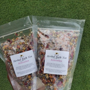 May include: Two clear plastic bags filled with a herbal bath tea blend. The bags are labeled "Herbal Bath Tea Relaxation" and include a list of ingredients: Epsom salt, Himalayan pink sea salt, rose petals, lavender buds, chamomile flowers, calendula flowers, lavender essential oil & lavender essential oil.