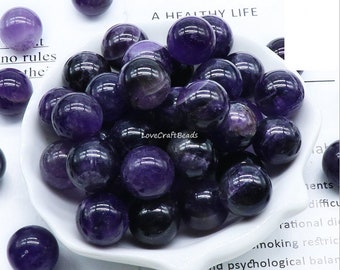 May include: A white bowl filled with approximately 20 small, round, purple amethyst beads. The beads are smooth and polished, with a slight variation in colour and pattern.