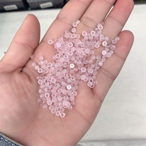 May include: A large pile of small, pale pink, round beads. The beads are translucent and have a slightly glossy finish.