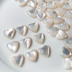 May include: A collection of white heart-shaped mother of pearl shell embellishments.
