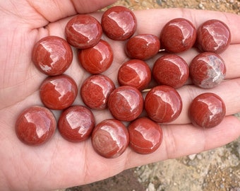May include: A collection of 17 smooth, polished red jasper stones, each with a unique pattern of white and red veins. The stones are arranged in a hand, showcasing their natural beauty and variation.