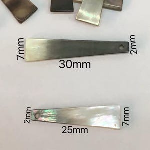 以下が含まれることがあります： イリデセント長方形の真珠母貝ペンダント。ペンダントは長さ30mm、幅7mm、厚さ2mmで、一端に小さな穴があります。別のペンダントは長さ25mmです。ジュエリー作りに最適です。
