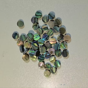 May include: A collection of iridescent abalone shell guitar tuning pegs. The pegs are round and have a variety of green, blue, and gold colors.