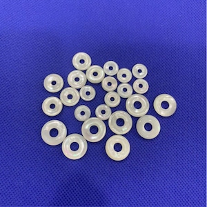 May include: A collection of white iridescent shell rings, some with a slight pearlescent sheen. The rings are various sizes and are arranged in a cluster on a blue background.