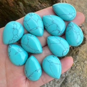 May include: Ten turquoise teardrop-shaped cabochons with a blue-green color and black veining. The stones are smooth and polished.