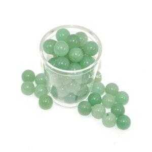 May include: A glass jar filled with green jade stone spheres. The spheres are scattered around the jar on a white surface.