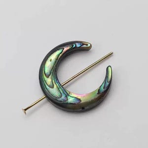 May include: A crescent-shaped hair slide with iridescent abalone shell inlay. The slide has a gold-coloured pin through the centre. The shell displays green, blue, and purple hues. This is a hair accessory.