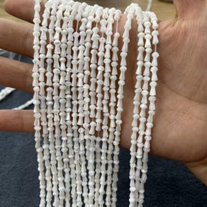 May include: A strand of white shell beads with a teardrop shape. The beads are strung on a clear thread and have a slight iridescent sheen.