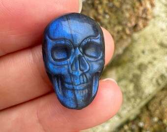 Puede incluir: Una talla de calavera de labradorita azul. La calavera está detallada con cuencas de ojos, nariz y boca talladas.