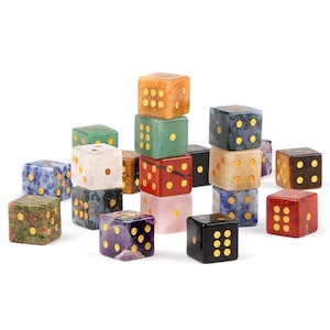 May include: A collection of colorful gemstone dice. The dice are various colors, including green, red, blue, and purple, with gold-colored dots. The dice are arranged in a scattered pile, with some stacked on top of each other.