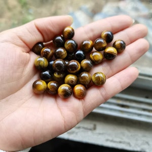 Peut inclure: Un ensemble de perles en œil de tigre dans différentes nuances de brun et d'or. Les perles sont rondes et lisses, avec un léger éclat.