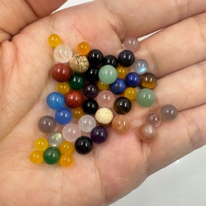 Op de afbeelding: Een verzameling kleurrijke edelsteen kralen in verschillende vormen en maten. De kralen zijn gerangschikt in een hand, waardoor hun natuurlijke schoonheid en unieke patronen worden getoond.