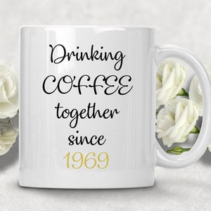 May include: White ceramic coffee mug with black text that reads "Drinking Coffee together since 1969". The year 1969 is in gold lettering.