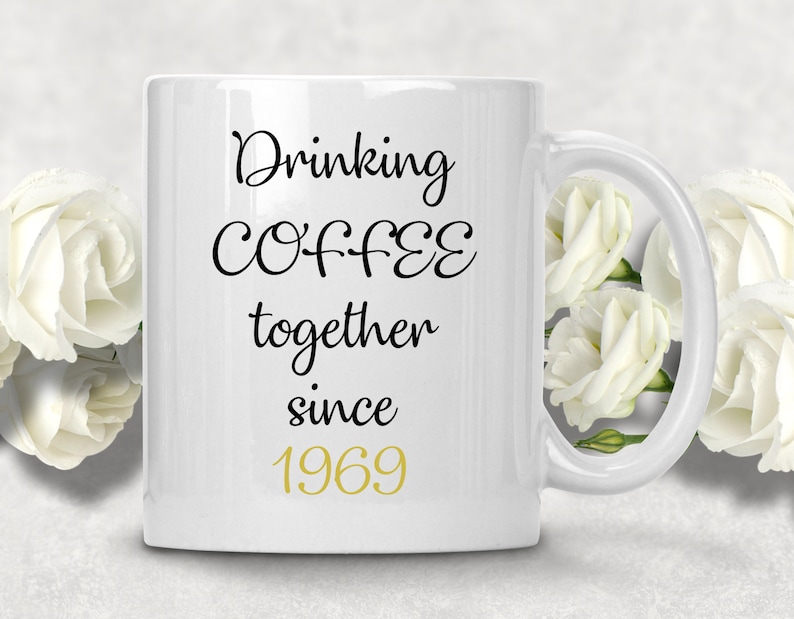 May include: White ceramic coffee mug with black text that reads "Drinking Coffee together since 1969". The year 1969 is in gold lettering.