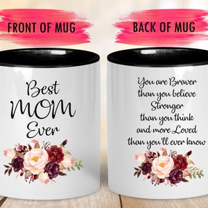 May include: White ceramic mug with a black handle and rim. The front of the mug reads "Best MOM Ever" with a floral design. The back of the mug has a quote about strength and love, also with a floral design.